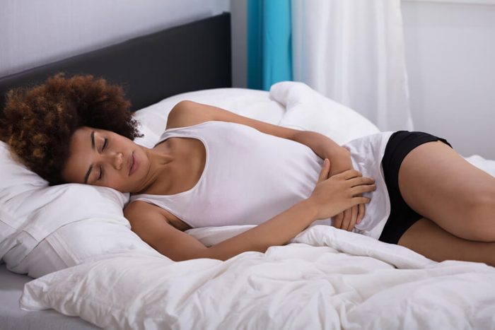 Young Woman Suffering From Stomach Pain Lying On Bed In Bedroom
