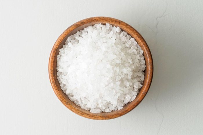 Wooden bowl with large sea salt scrub on gray stone table.