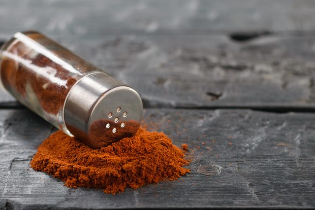 Ground chili is poured from a jar on a dark wooden table.