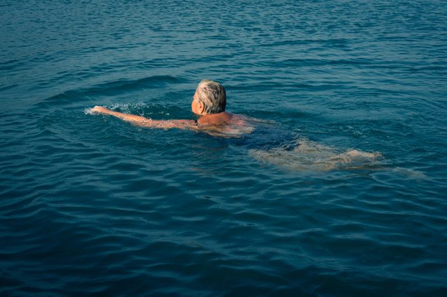Old, short white haired woman swimming alone in dark blue water.