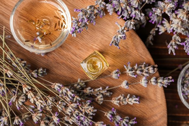 Glassware with essential oil and lavender on wooden board