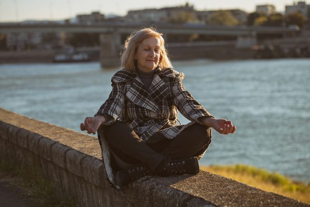 Senior woman enjoys meditating by the river.Toned image.