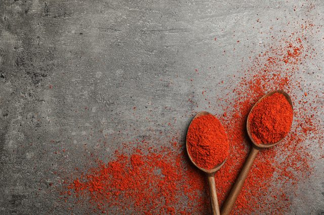 Spoons and powdered chili pepper on gray background, top view with space for text