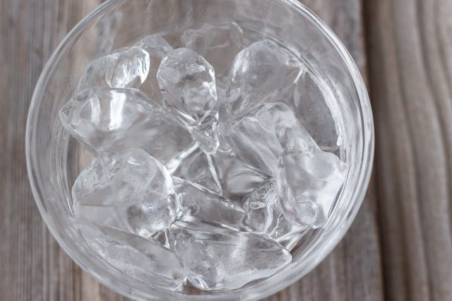 horizontal image of a clear glass bowl with ice cubes on a wooden background