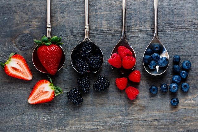 Top view of berries mixed (strawberries, raspberries, blueberries and blackberries) on vintage metal spoons over dark wood. Agriculture, Gardening, Harvest Concept. Background with space for text.