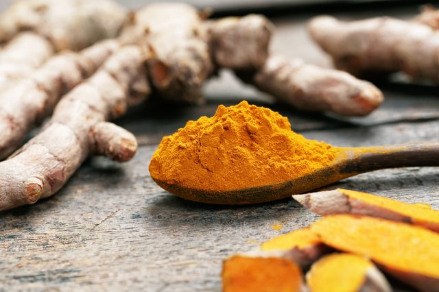 Turmeric powder and turmeric on wooden spoon.