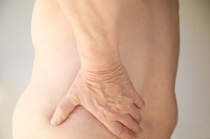 A shirtless man has his hand on his sore back.