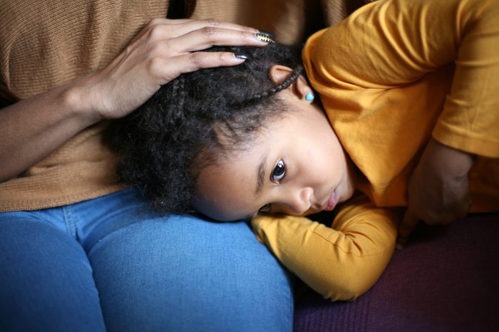 Little girl resting her head on her mother's lap.