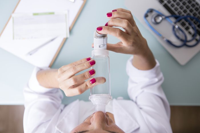 Person inhaling medication from a pressurized cartridge inhaler