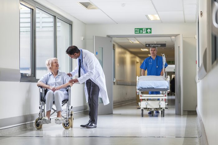 Male nurse pushing stretcher gurney bed in hospital corridor with doctor & senior female patient
