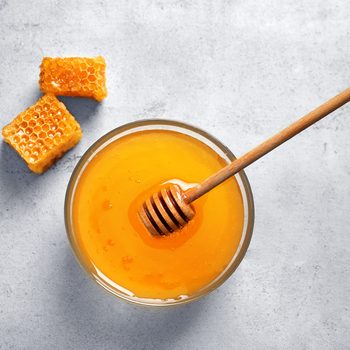 Glass bowl with delicious honey and dipper on table