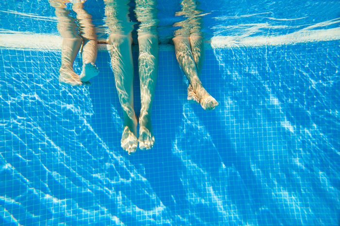 3 pairs of feet under water in a swimming pool