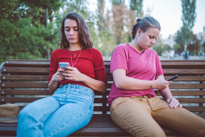 two friends sitting on a bench ignoring each other