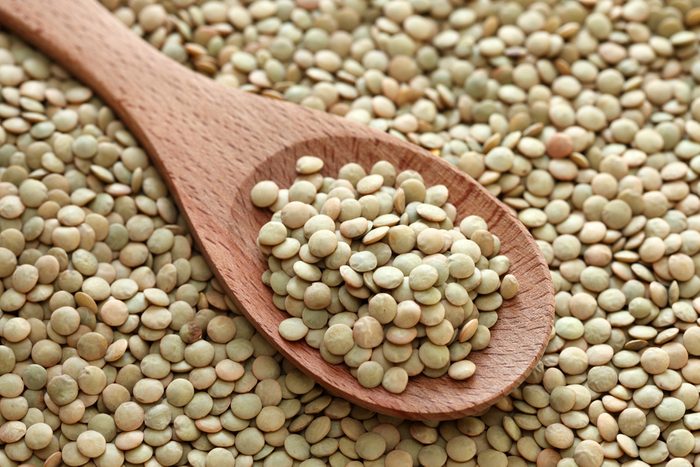 Green lentils in a wooden spoon on green lentils background. Close-up.