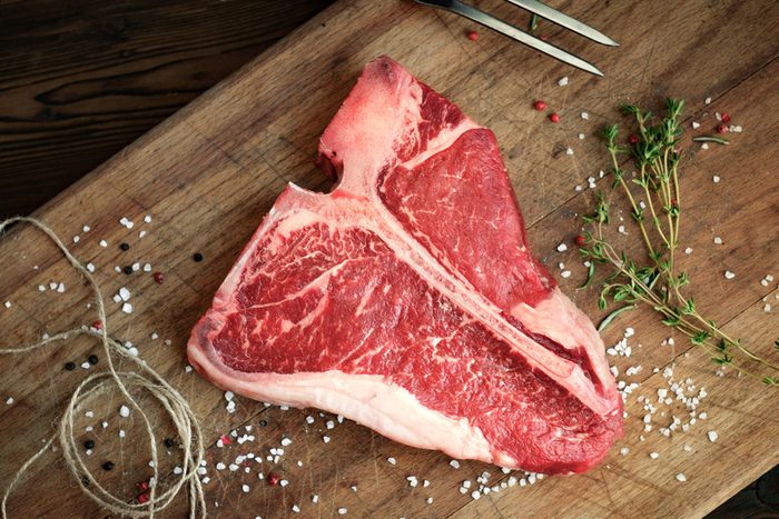 raw t bone steak of beef on the butcher's Board with pepper, salt, herbs, close twine, top view