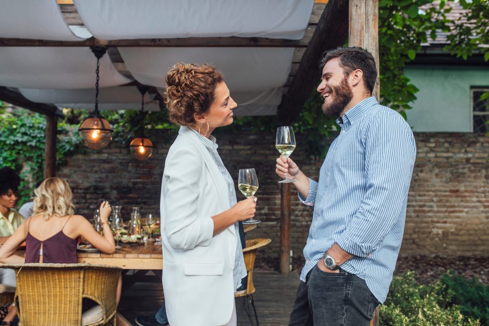 Pretty Caucasian woman and her man friend standing at terrace and chatting and drinking wine.
