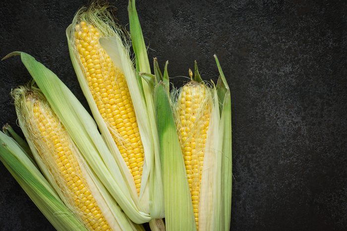 Ripe young corn cob with leaves on black concrete background, copy space.