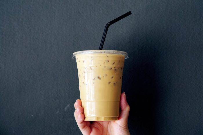 Woman holding plastic glass of iced coffee with milk on grey background