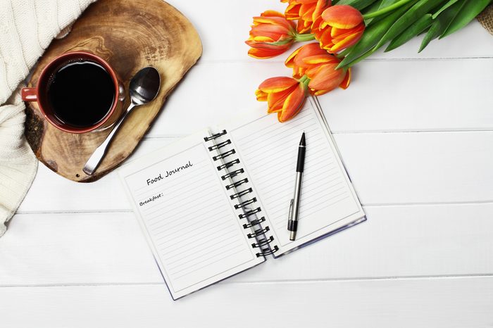 Overhead shot a cup of coffee, food journal, and bouquet of tulips.
