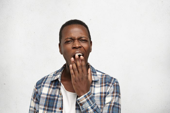 Young man covering mouth while yawning.