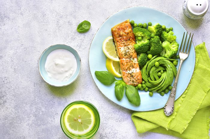 Grilled salmon garnished with green vegetables on a blue plate.