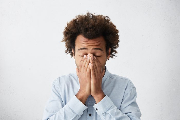Young male covering his face with hands, eyes closed. 