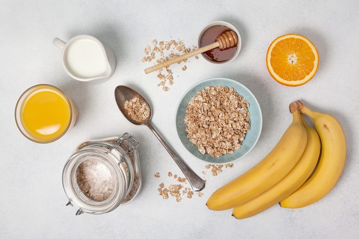 Oatmeal, milk, honey, orange, orange juice, bananas on a white countertop