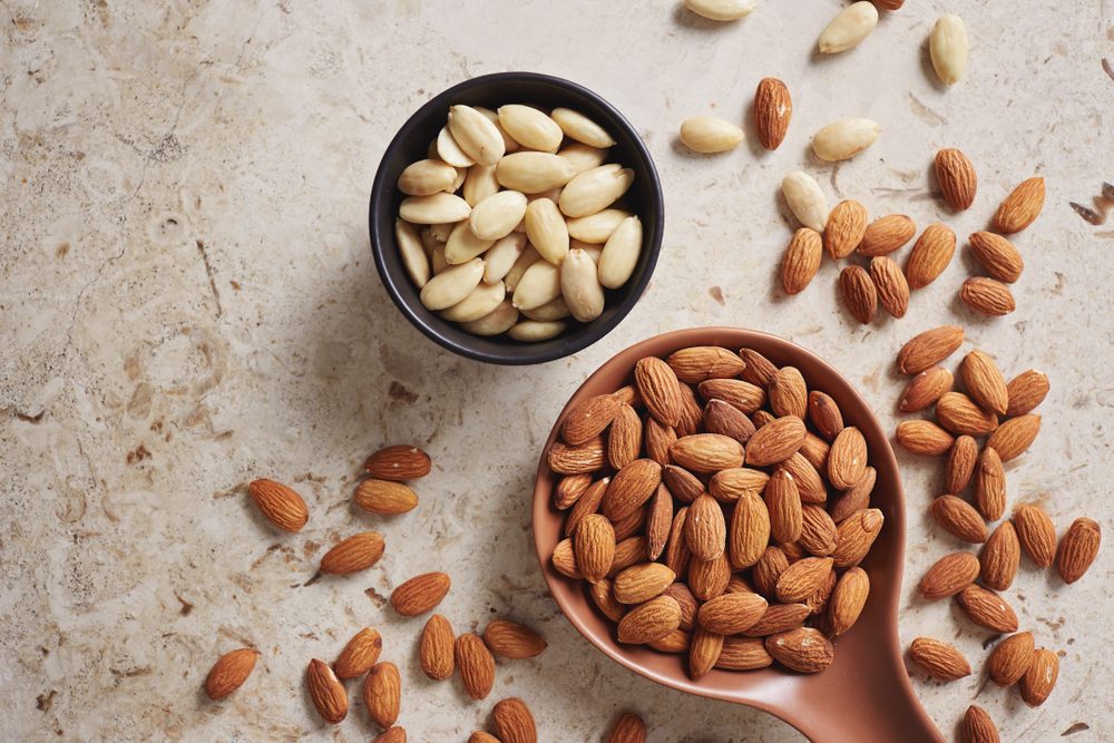 Peeled (blanched) and unblanched whole almonds. Shelled almonds on a spoon with a small black bowl of blanched almonds.