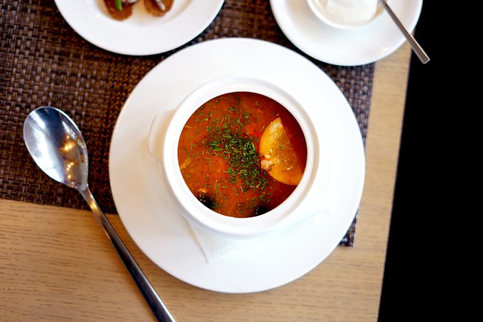 Soup saltwort with lemon, meat, pickles, tomato sauce olives in a bowl on a sacking, bread on a wooden board background
