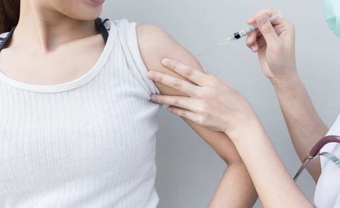 Nurse holding a syringe with a liquid inside next to a female arm.