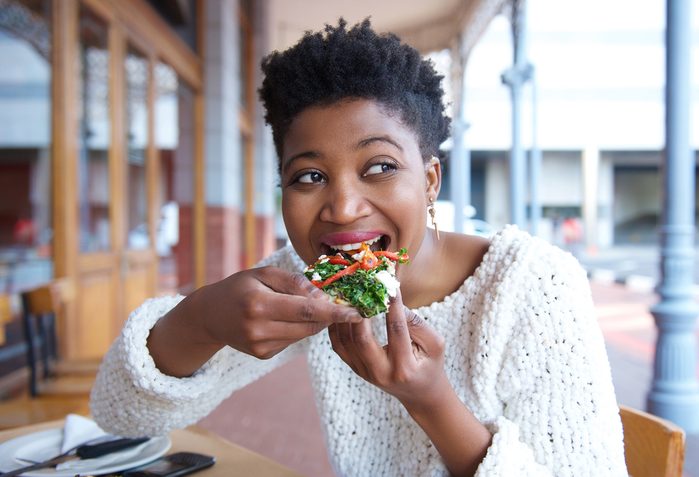 Close up portrait of a happy young woman eating pizza at restaurant