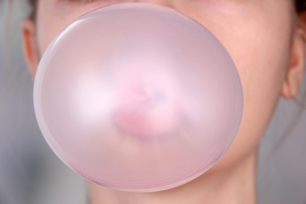 Person doing bubble with chewing gum on bright background