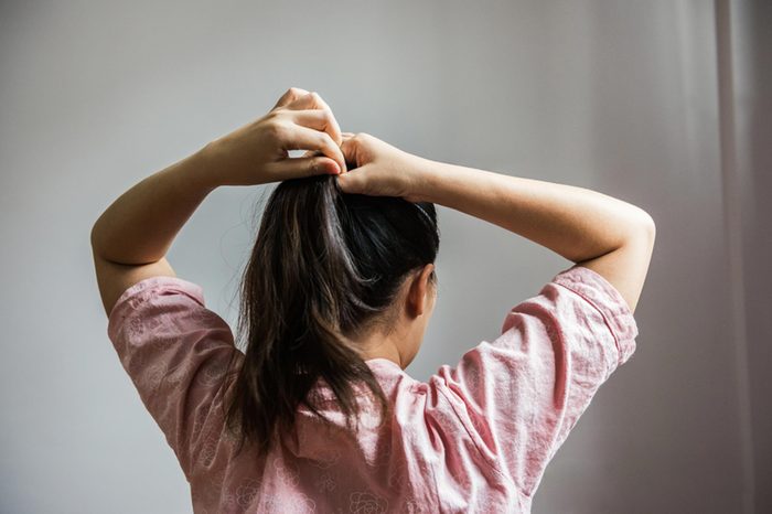woman from the back, putting up her hair in a ponytail