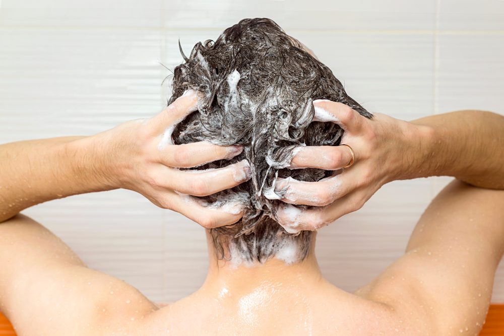 young manis washing his hair, taking a shower with foam on his head holds fingers in hair in bathroom, he use shampoo, attractive young guy is cleaning his body, health care concept