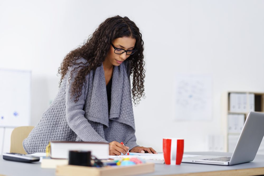 Young African American design artist at work in her studio standing at her table sketching on a pad with colored crayons