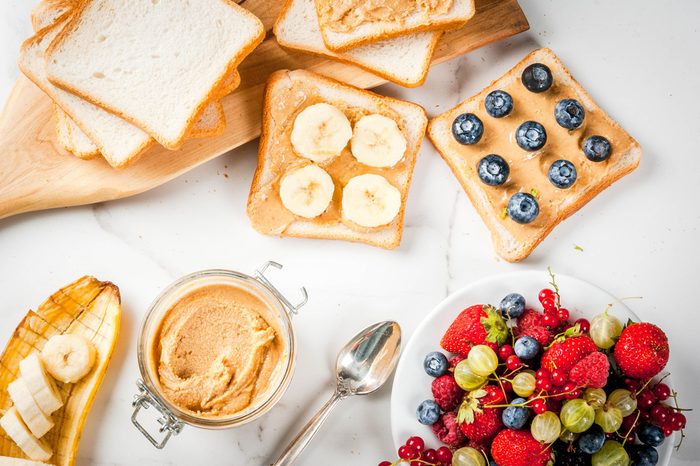 Traditional summer breakfast: sandwiches of toast with peanut butter, berry, fruit apple, peach, blueberry, blueberry, strawberry, banana on a white marble table.