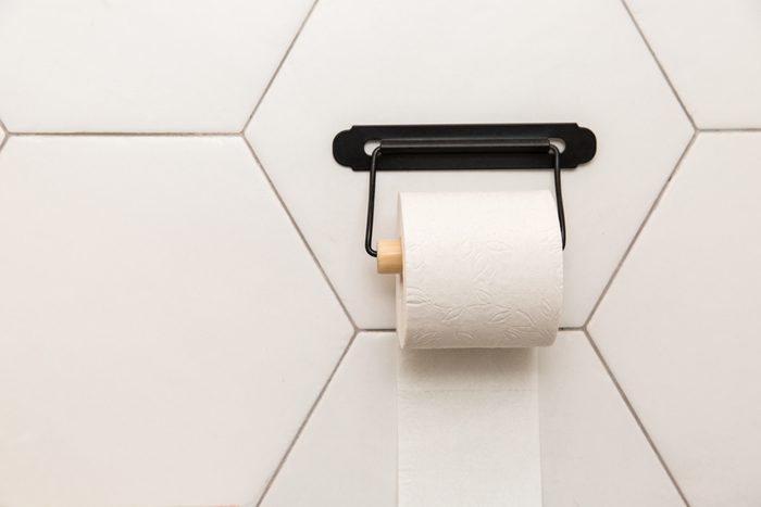 A white roll of soft toilet paper neatly hanging on a modern chrome holder on a light bathroom wall.