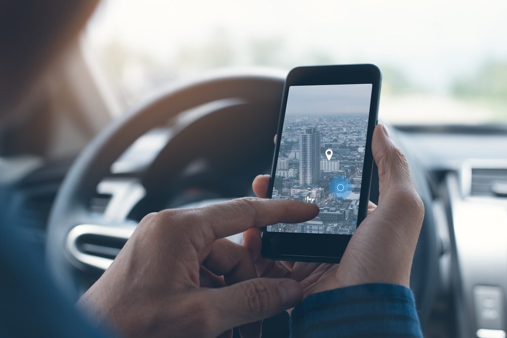 Man searching destination direction or address on gps or navigator application via mobile smartphone inside a car while driving car, close up