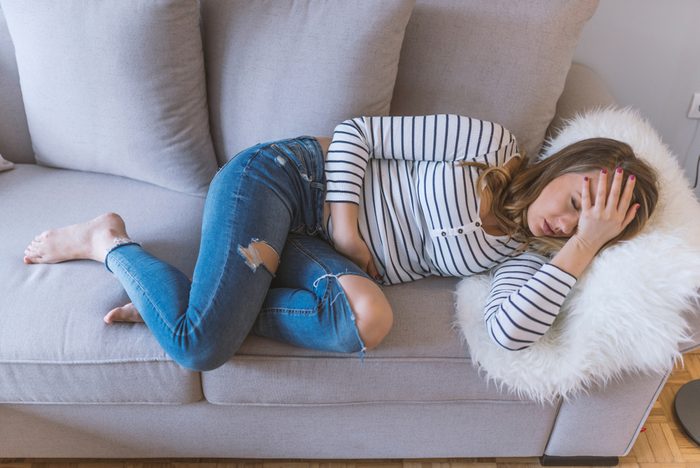 Young beautiful woman having painful stomachache. Woman with menstrual pain is holding her aching belly - body pain concept. woman having abdominal pain, upset stomach or menstrual cramps.