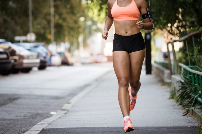 Runner listening to music while jogging on sidewalk.