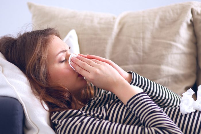 Portrait of a sick woman blowing her nose while sitting on the sofa 