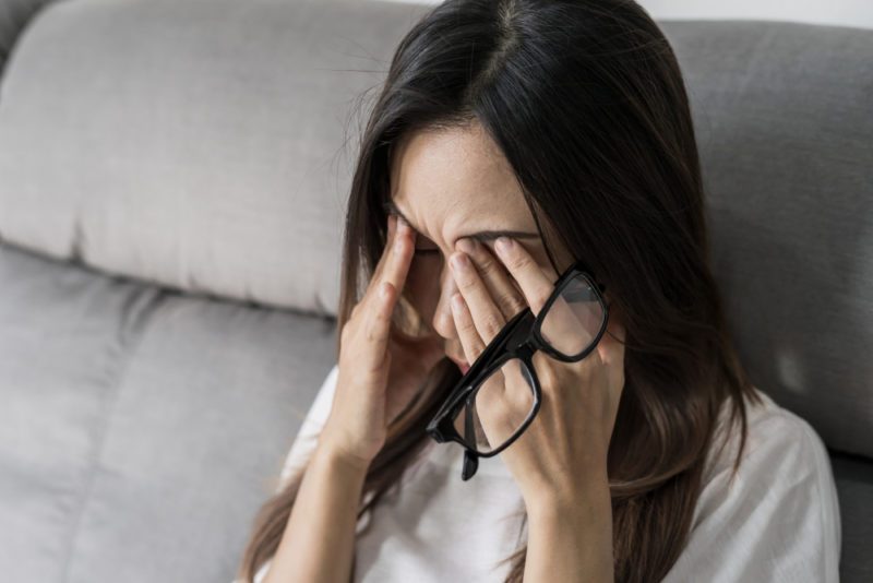Young woman rubbing her eyes feel painful and take off her glasses siiting on sofa and rest one's eyes at home
