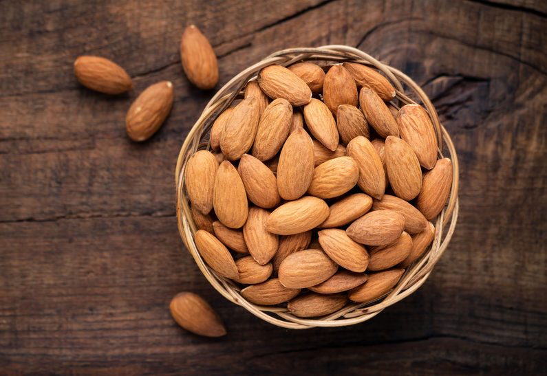 Almonds in willow bowl against dark rustic wooden background. Overhead view