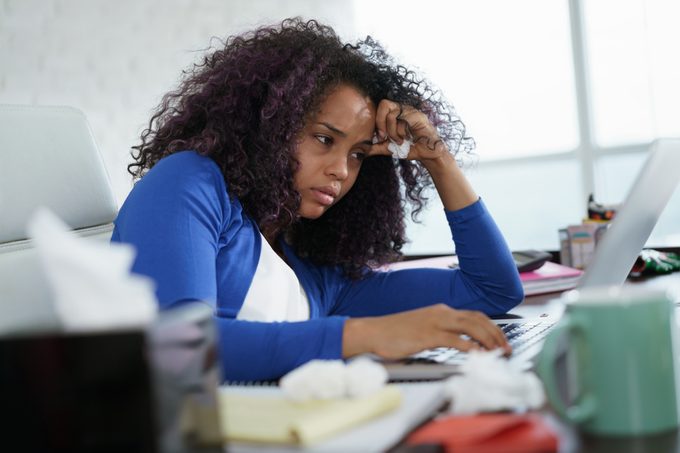 Sick african american girl working from home office. Ill young black woman with cold, sitting at desk with laptop computer and sneezing for allergy.