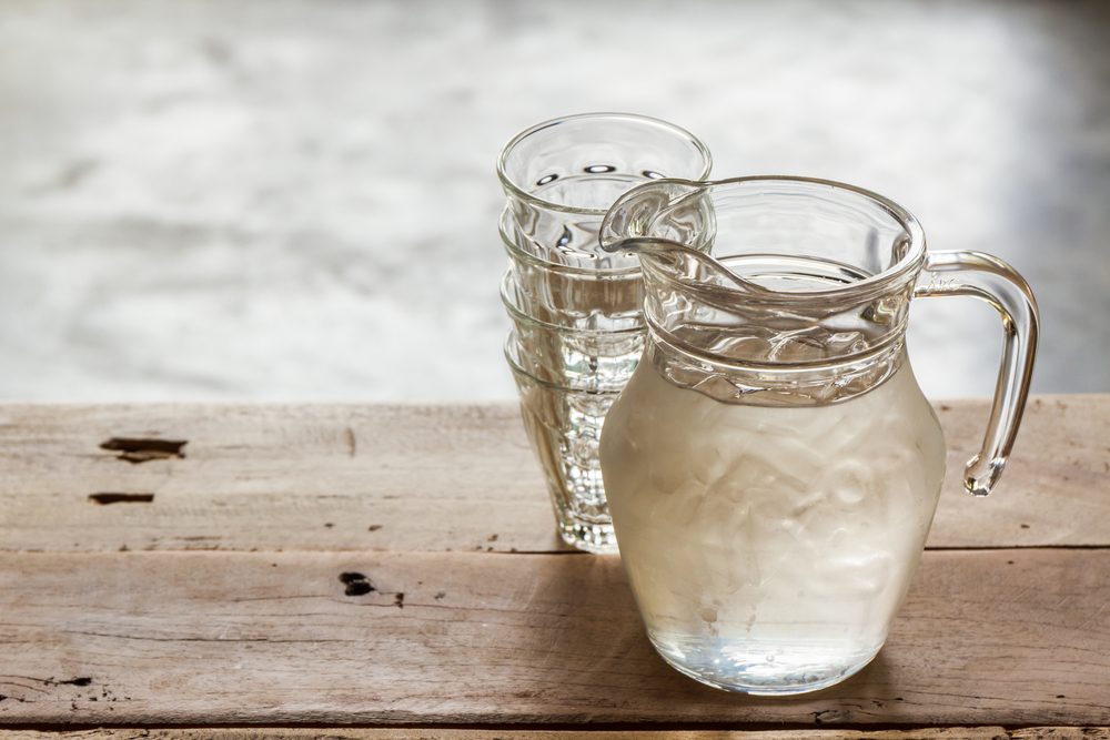 Glass pitcher of water and glass on wooden table background.