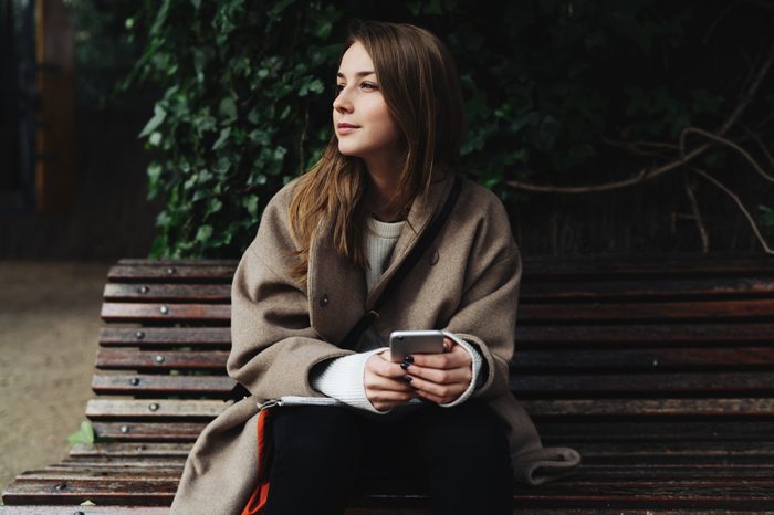 Hipster girl with her phone on a park bench