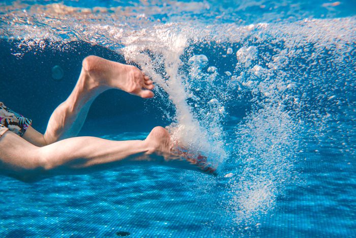 Men's legs swimming underwater in the swimming pool in summer