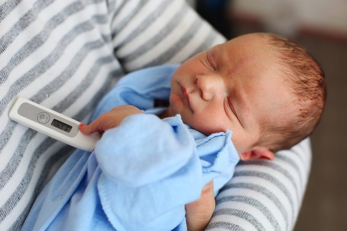 Newborn baby boy in parent's arms with thermometer