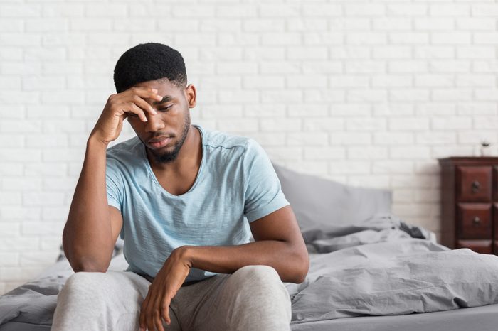 Bad mood in morning. Young depressed african-american man sitting on bed and consider about problems, copy space