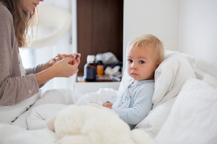 Mother and baby in pajamas, early in the morning, mom taking care of her sick toddler boy. Baby in bed with fever and running nose